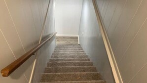 Eine schmale Treppe mit hölzernem Geländer, Teppichstufen und hellen Wänden.