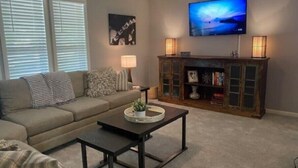 Una sala de estar con un sofá, una mesa de centro, un televisor y un mueble con objetos decorativos.