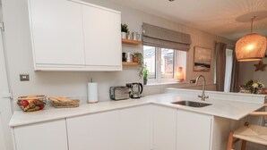 A modern kitchen with white cabinetry, a built-in island with a sink, and a wooden herringbone floor. - Driftwood Sands (Chathill)