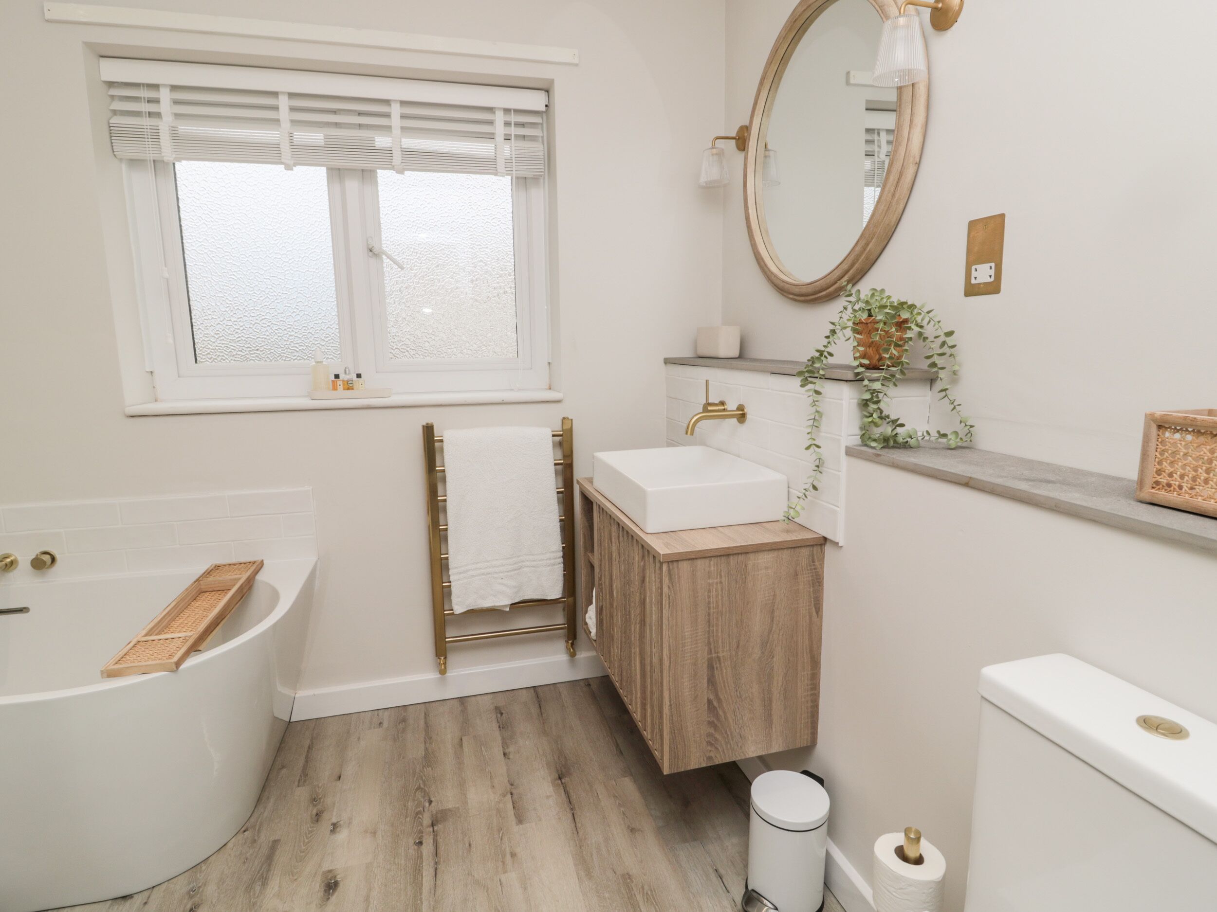 A bathroom with a bathtub, a sink, a toilet, a window with blinds, and a mirror.