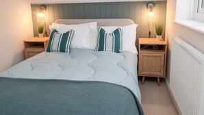 A neatly arranged bedroom with a bed, two bedside tables, a nightstand, a radiator, and two wall-mounted lamps. - Driftwood Sands (Chathill)