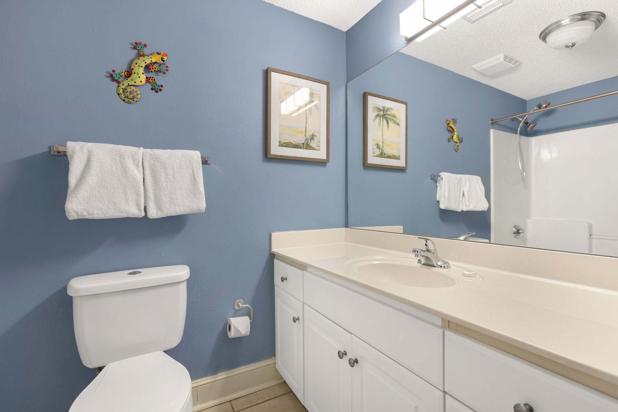 A bathroom with a toilet, sink, and mirror. There are towels hanging on the wall and a shower area.