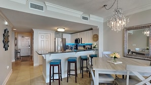 A modern kitchen with a central island, bar stools, and a dining table with chairs. - Majestic Beach Towers I by Southern Vacation Rentals (Panama City Beach)