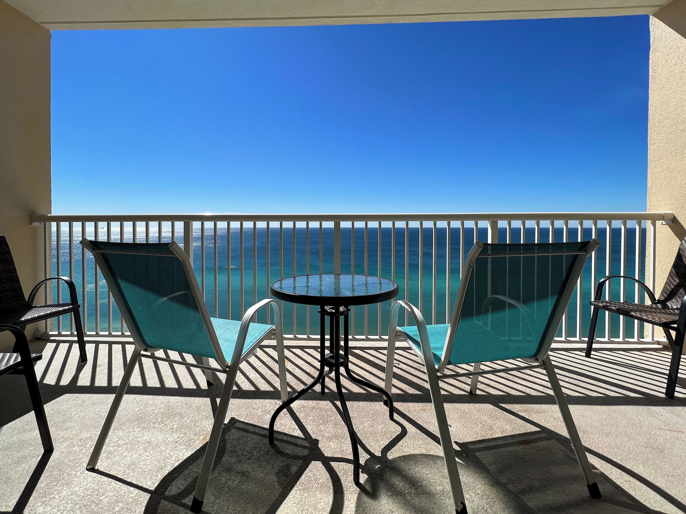 Un balcon avec une table et deux chaises, d’où l’on peut admirer un ciel bleu azur et l’océan.