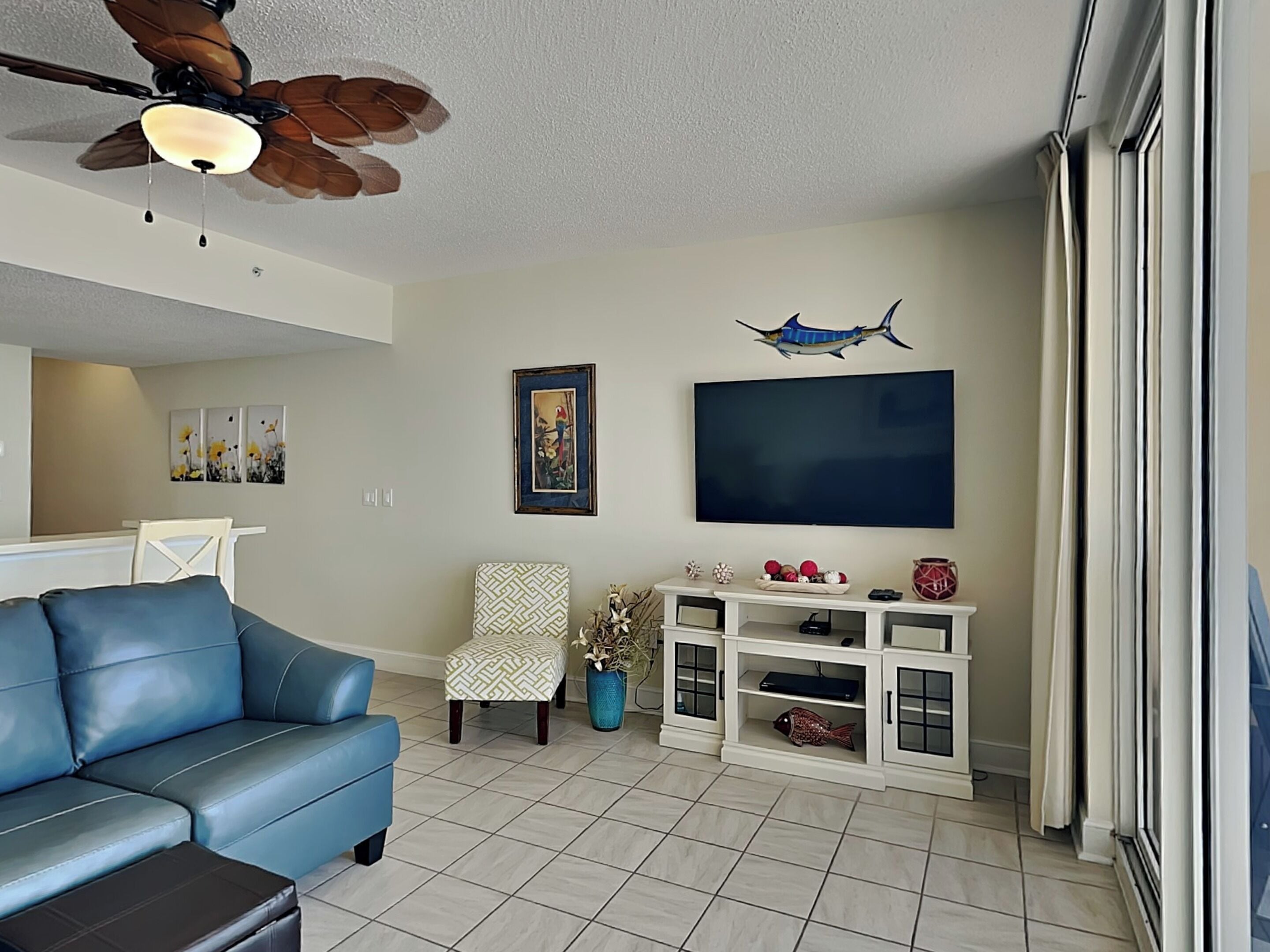 A living room with a blue sofa, a ceiling fan, a mounted TV, and a decorative fish on a cabinet.
