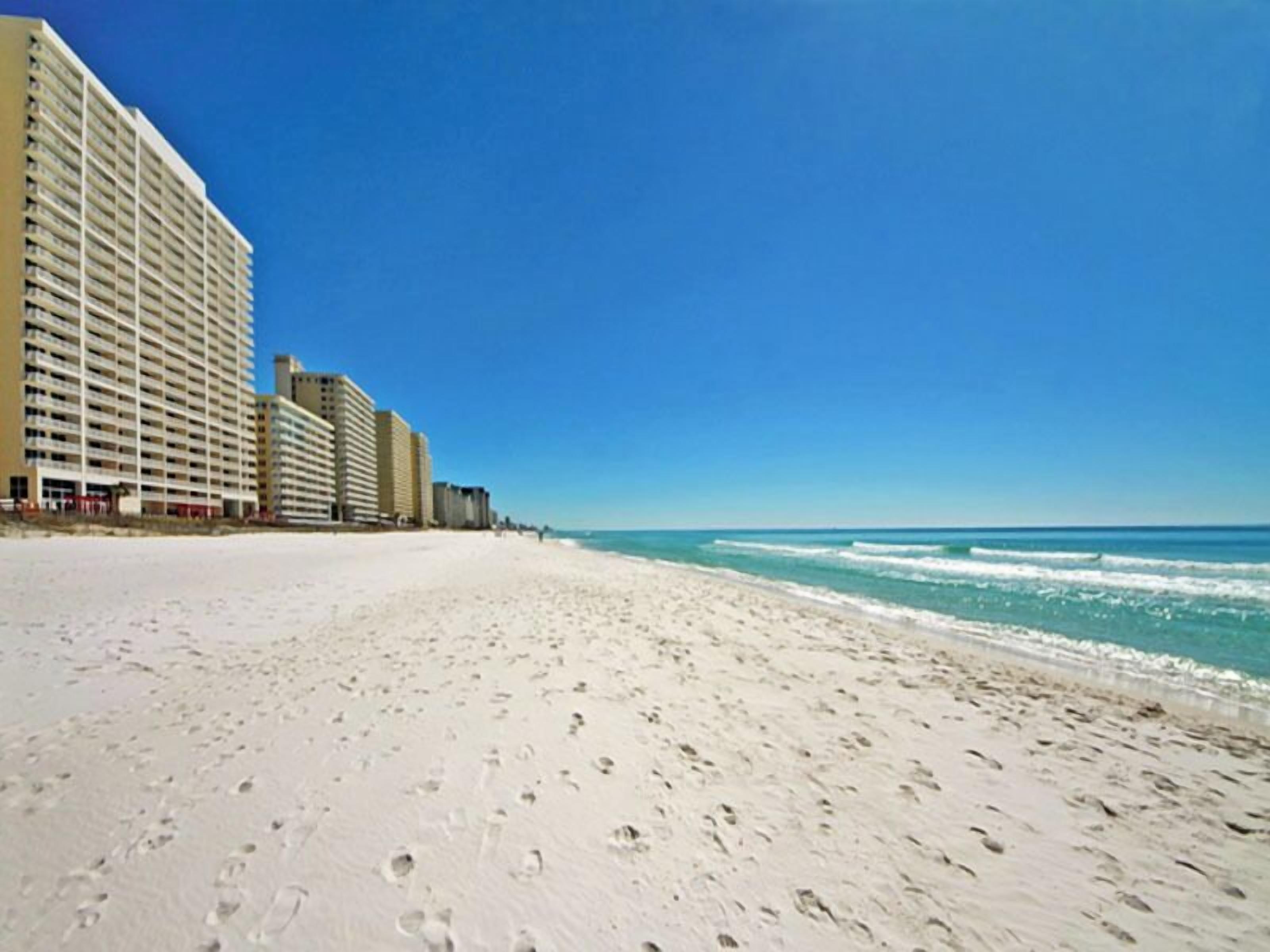 Un hotel frente a la playa con varios edificios altos, una playa de arena y olas oceánicas.