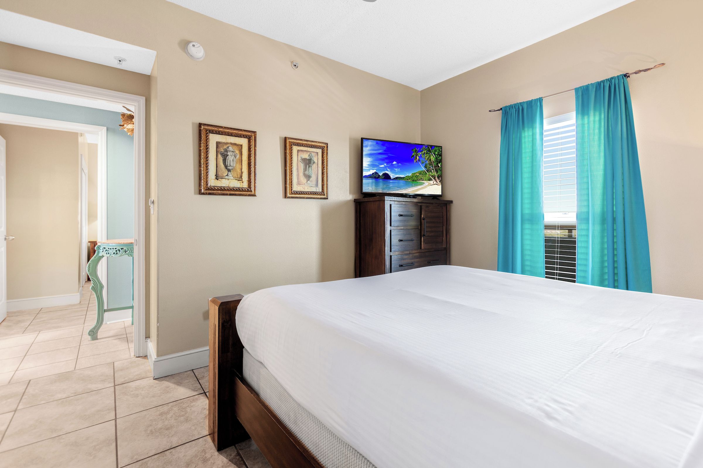 Une chambre à coucher avec un lit, un téléviseur posé sur une commode et une porte donnant sur une autre pièce.