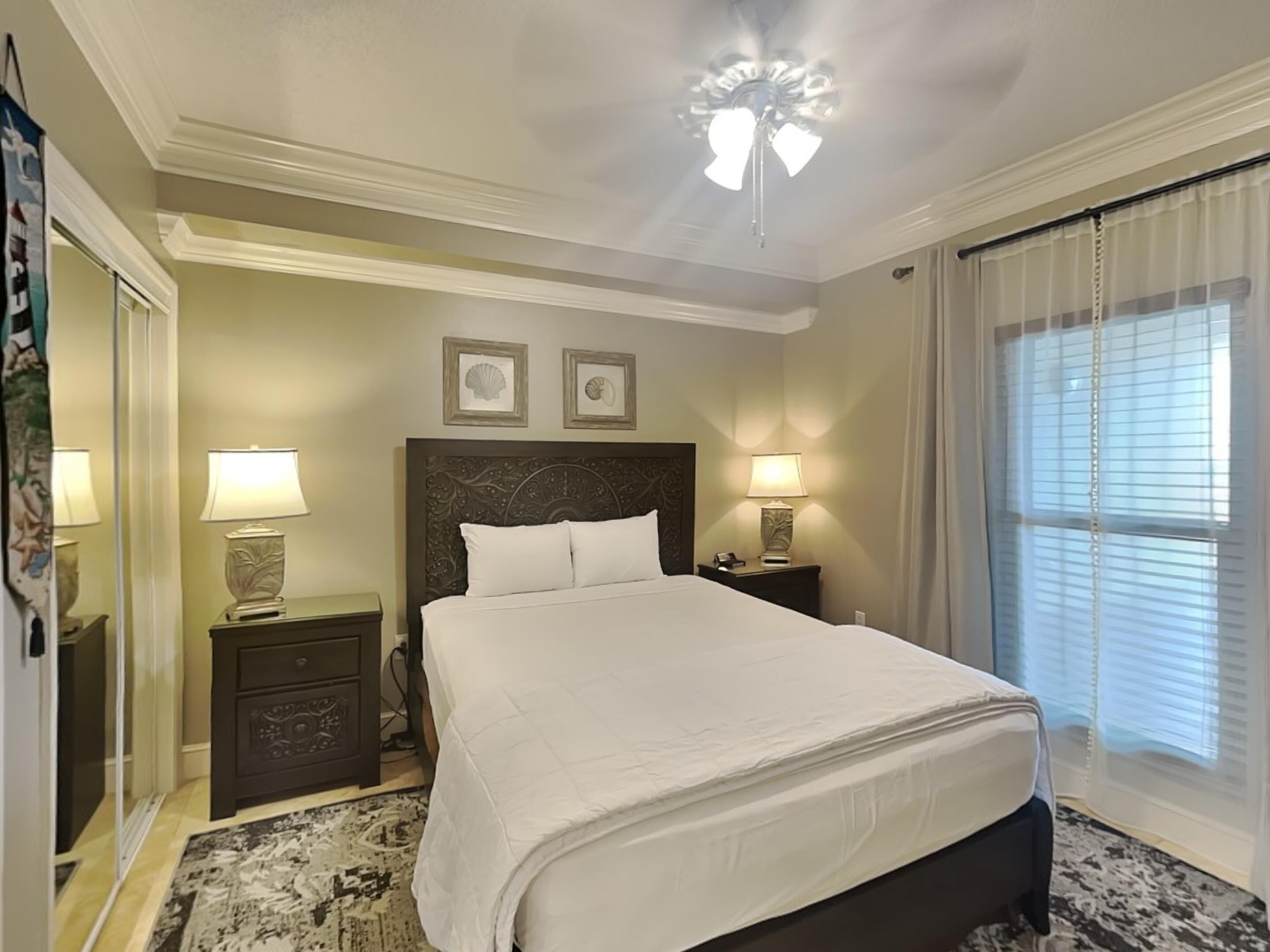 A hotel room with a large bed, two bedside lamps, a ceiling fan, and a window with blinds.