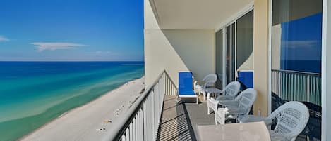 A balcony with a view of the beach and ocean, white wicker chairs, and a table.