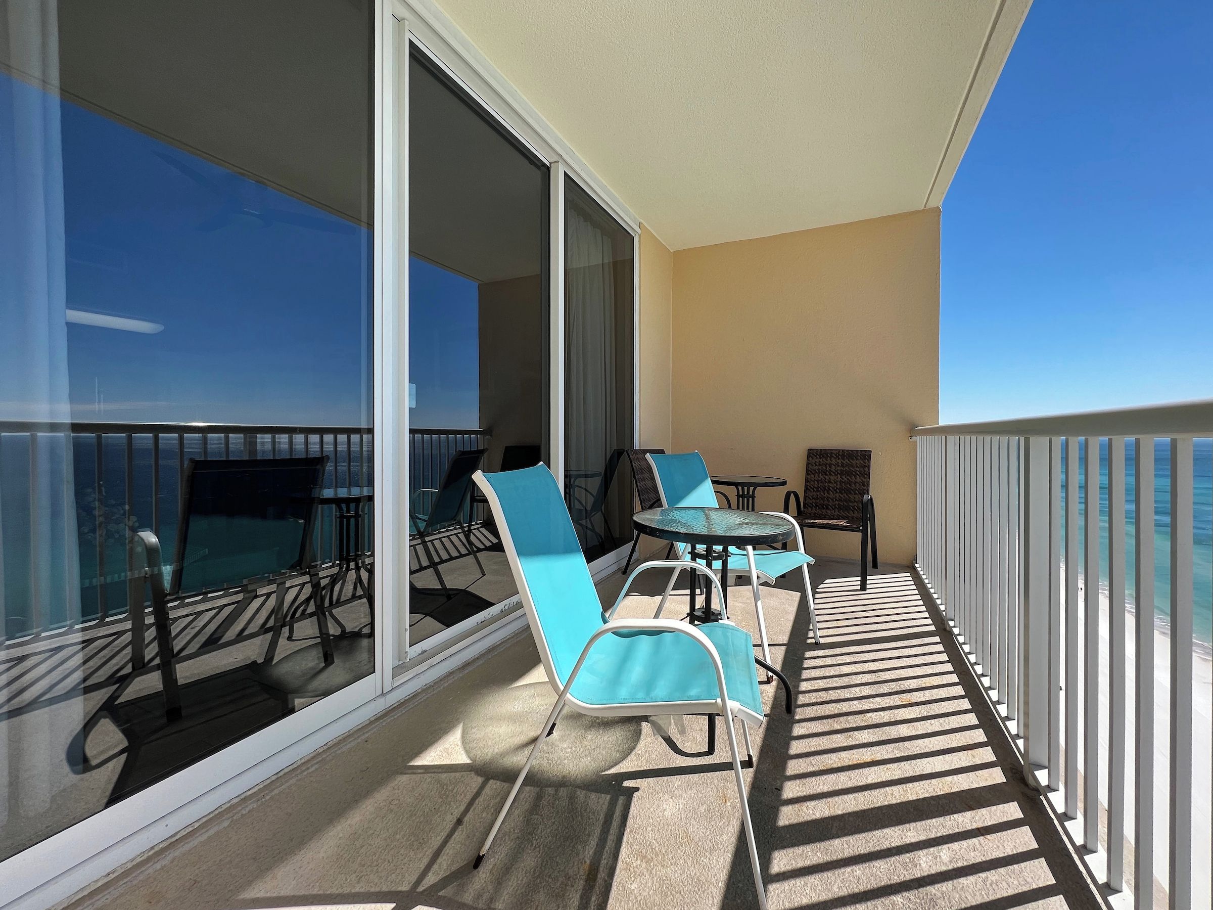 A balcony with a glass door, two chairs, a small table, and a view of the ocean.