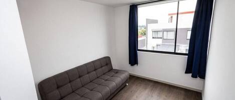 A room with a grey sofa, a large window with dark curtains, and a ceiling light fixture.
