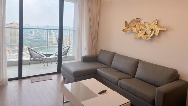 Ein modernes Wohnzimmer mit einem grauen Ecksofa, einem Couchtisch und Blick auf eine Stadtlandschaft durch große Fenster.