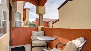 A balcony with a round table and two chairs, beige cushions, and a red-tiled roof.
