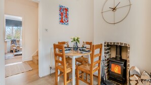 A dining area with a round table, wooden chairs, and a fireplace. - Sea Whispers Cottage (Poole)