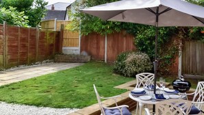 A patio with a table set for four, surrounded by white chairs with blue cushions. - Sea Whispers Cottage (Poole)