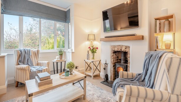 A cozy living room with a fireplace, striped armchairs, a coffee table, and a bookshelf. - Sea Whispers Cottage (Poole)