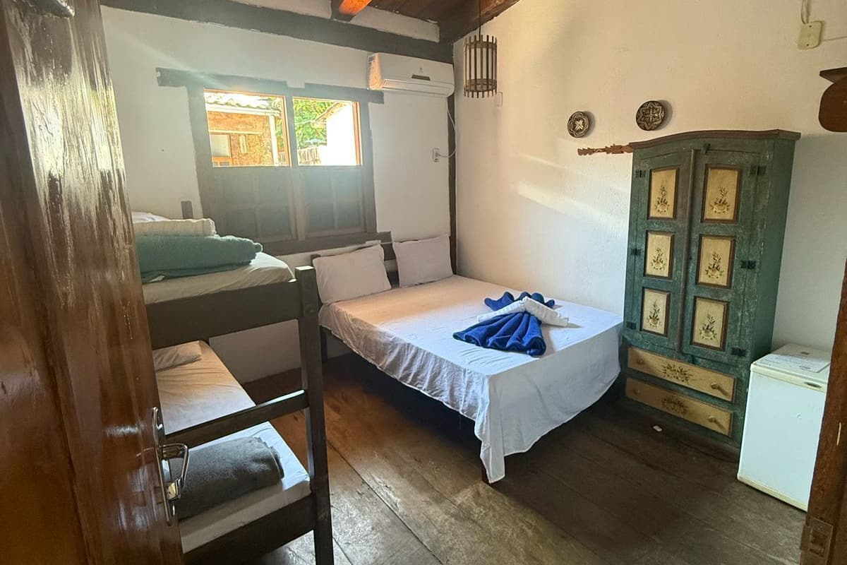 A small, rustic room with a bunk bed, a single bed, a wooden cabinet, and a window.