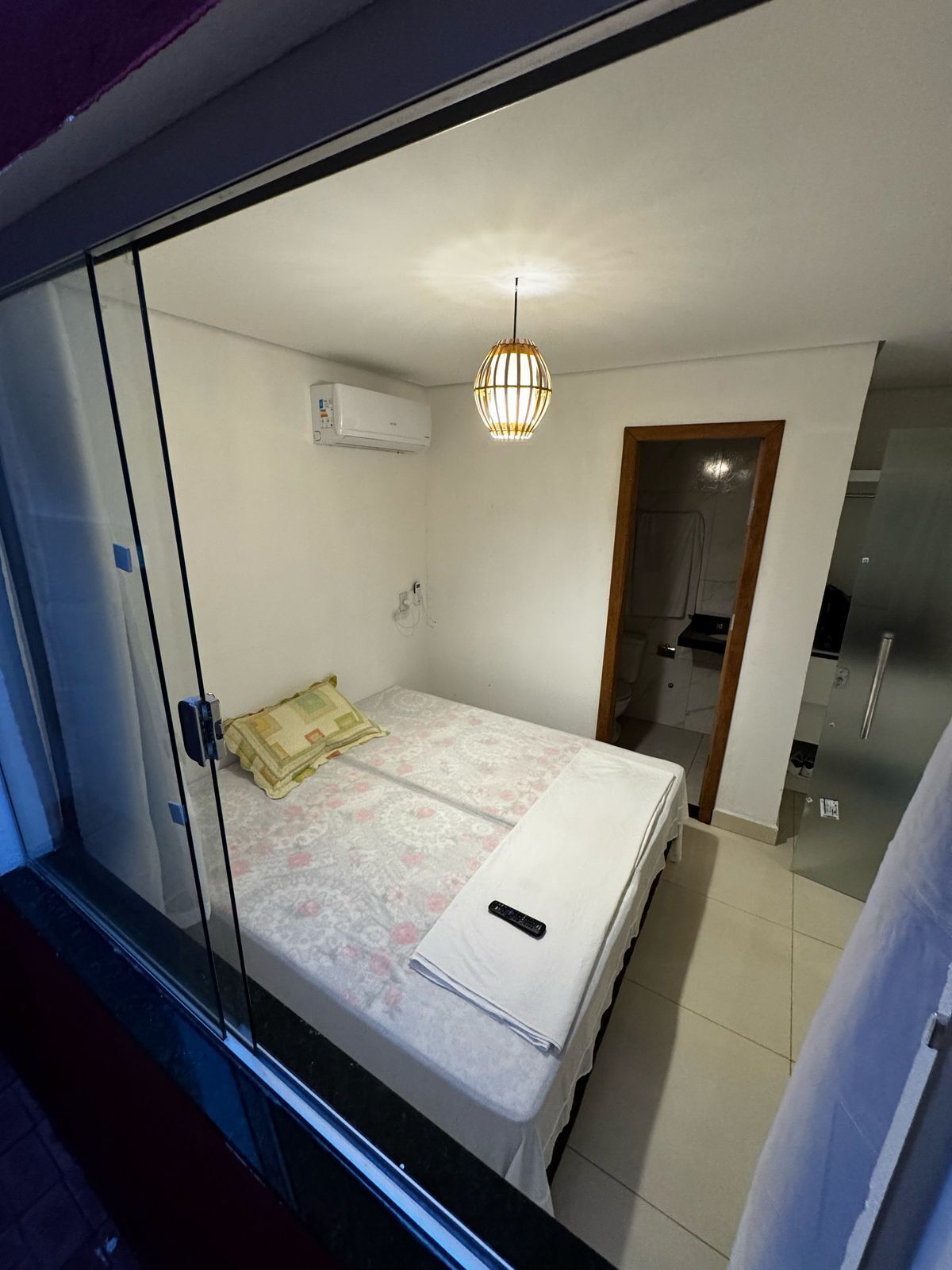 Un dormitorio con cama, aire acondicionado, lámpara colgante y puerta que da a una cocina.
