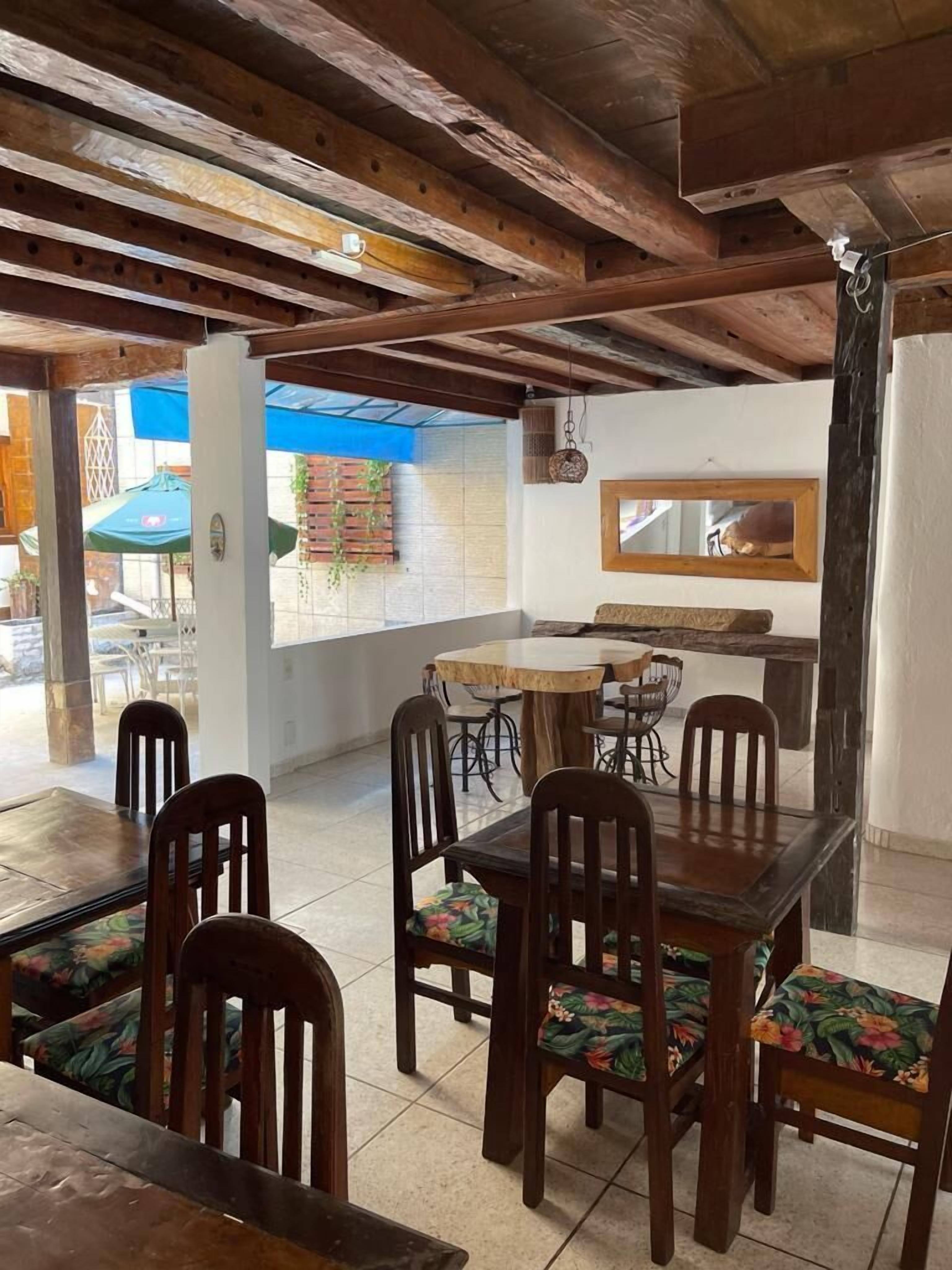 A dining area with wooden tables and chairs, a hanging light fixture, and a view of the outside through a window.