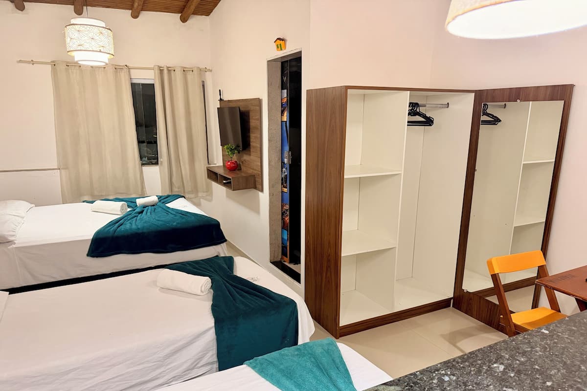 A hotel room with two beds, a wardrobe, a small table, and a mirror.