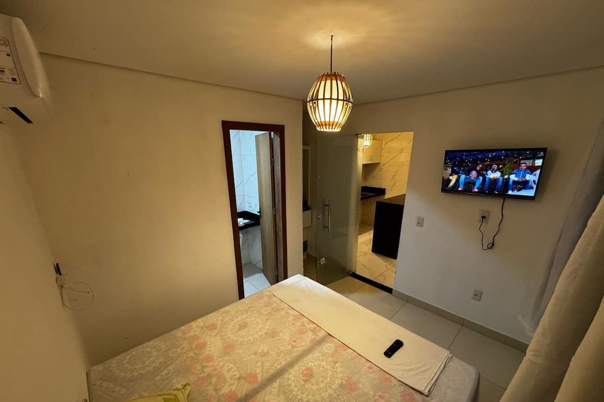 A bedroom with a bed, a television, a door leading to a bathroom, and a light fixture.