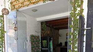 A modern entrance with a glass door, a stone-paved area, and a Monster Energy fridge. - Pousada Portal do Mucugê (Porto Seguro)