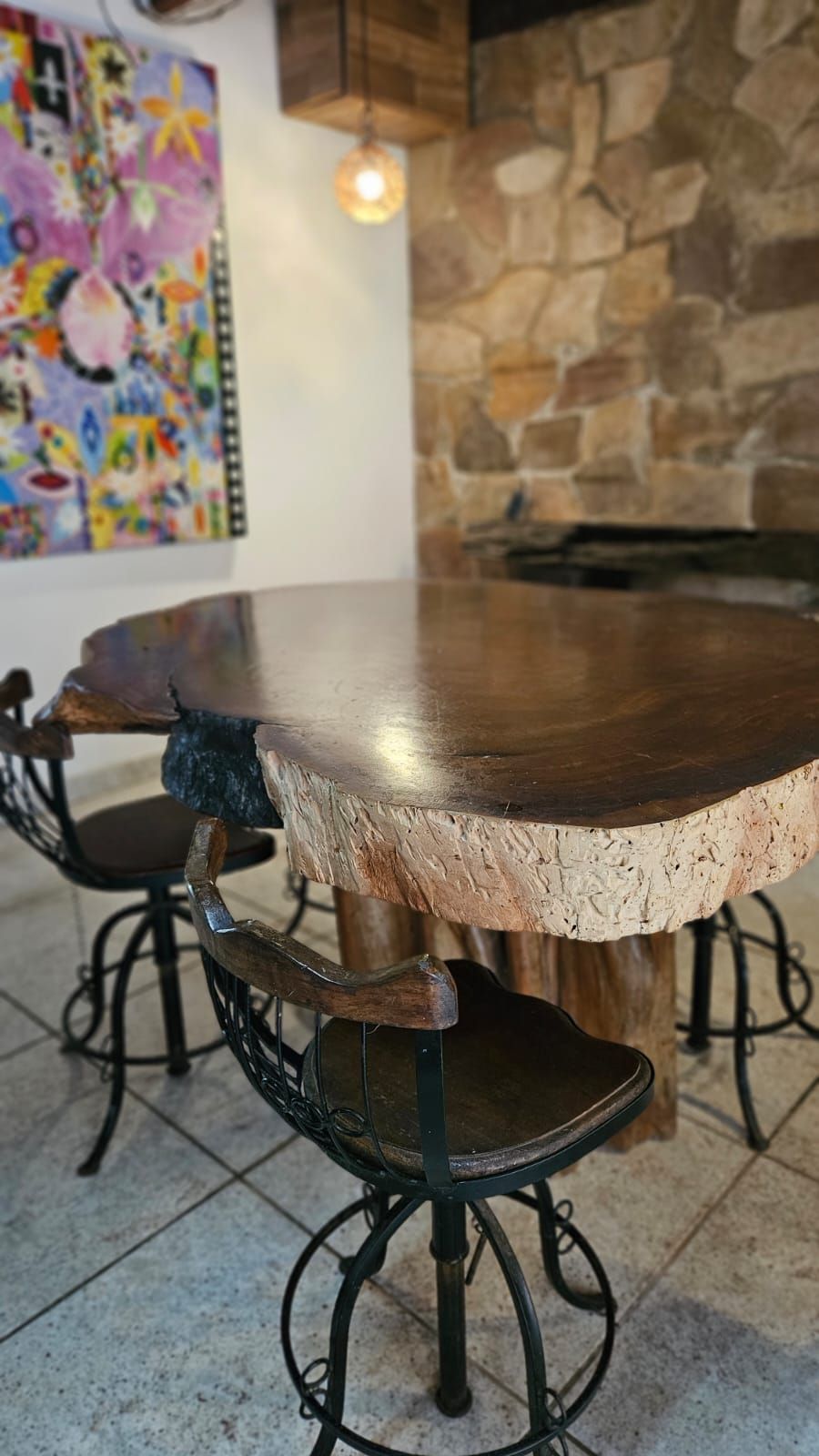 Mesa redonda de madeira com borda natural, rodeada por cadeiras de metal com design vintage.