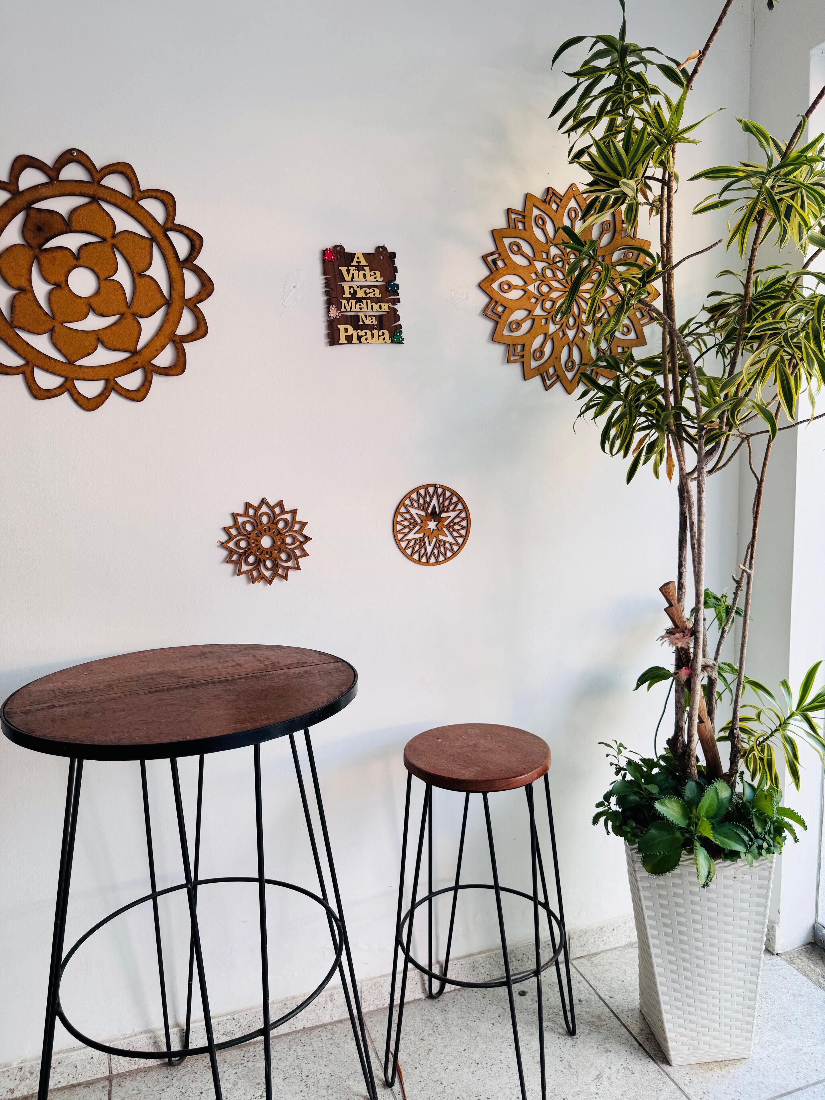 A wall with decorative metal wall art, two stools, and a potted plant.