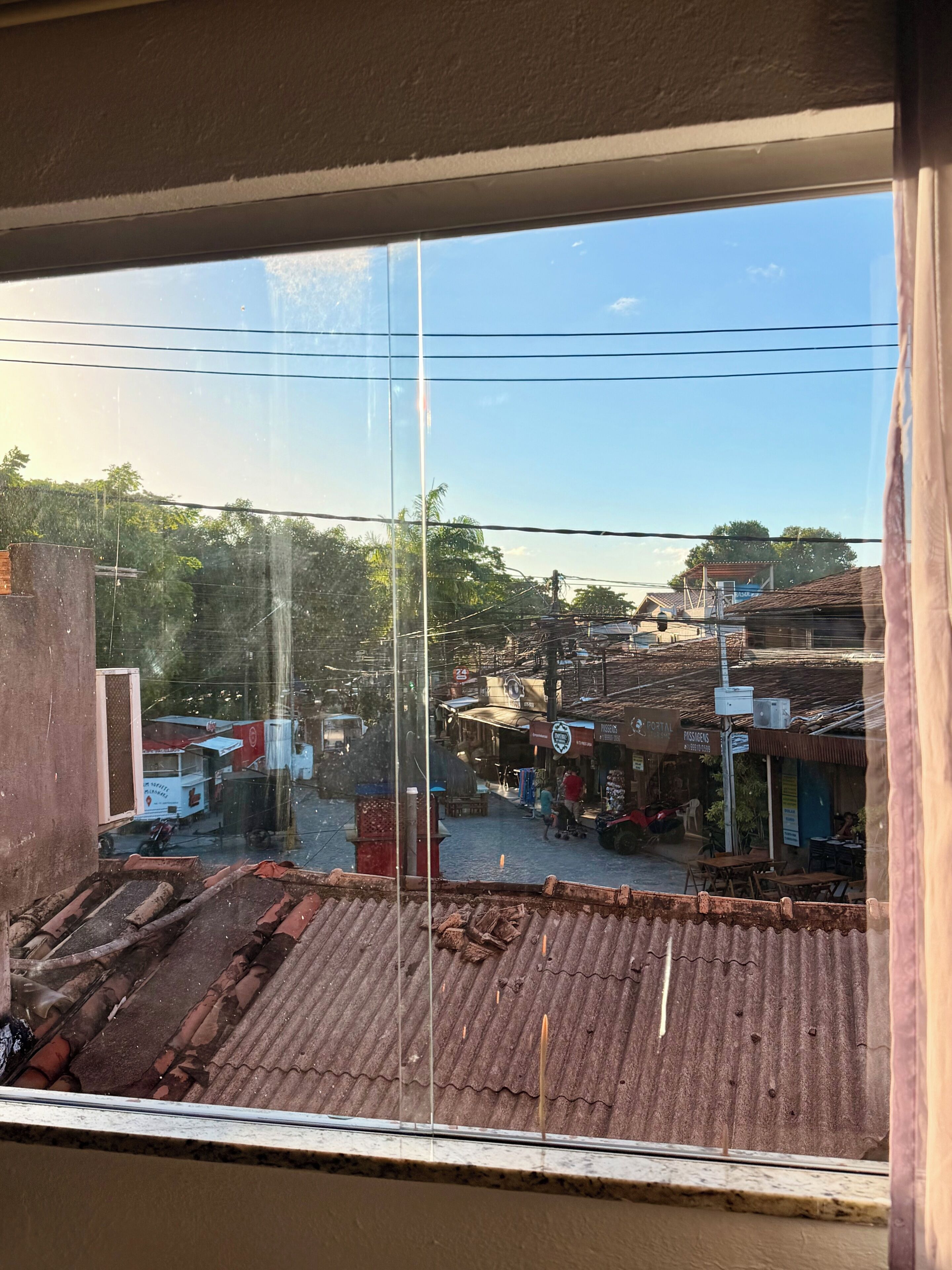 Vista a través de una ventana con cielo despejado, una calle con edificios y un letrero de comercio.