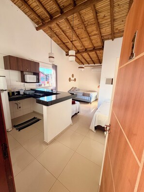 Cocina compacta con microondas, lavamanos y techo de madera.