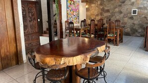 A rustic dining area with a large wooden table and chairs, a stone wall, and a colorful abstract painting. - Pousada Portal do Mucugê (Porto Seguro)