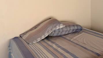 Uma cama com roupa de cama listrada, um travesseiro xadrez e um cobertor marrom.