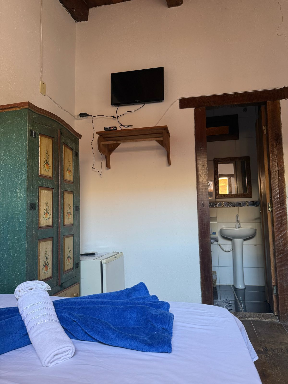 A bedroom with a bed, a wooden cabinet, a television, and a bathroom visible through an open door.