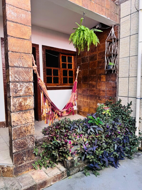 A stone building with a hammock, potted plants, and a hanging plant. - Pousada Portal do Mucugê (Porto Seguro)