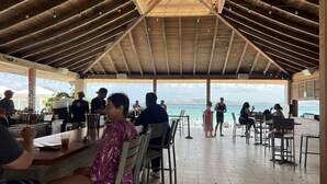 A covered outdoor dining area with wooden beams and string lights, overlooking a beach and ocean. - Sapphire Beach Retreat - Luxury Oceanfront Gem! (St Thomas)