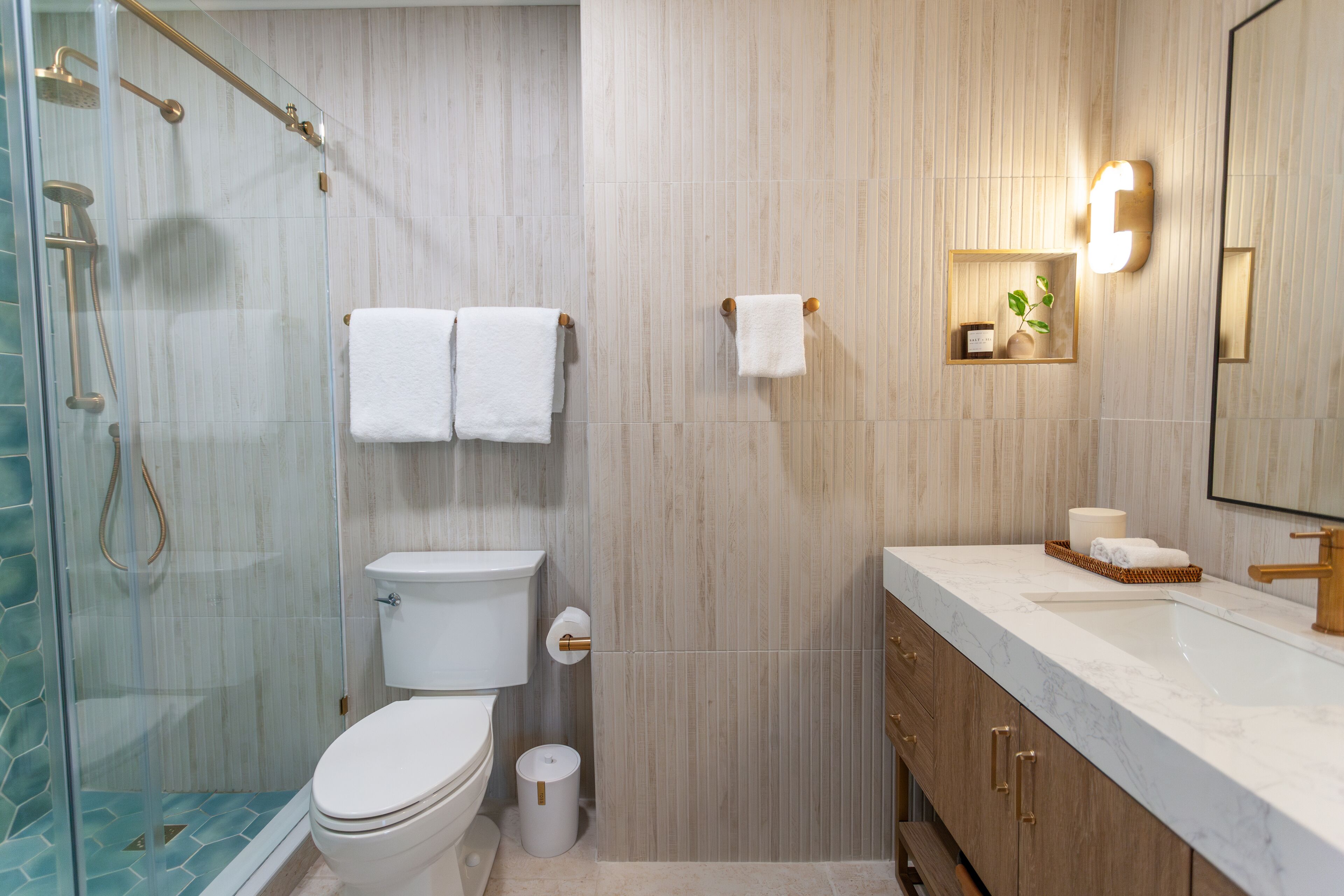 Ein modernes Badezimmer mit einer Duschkabine aus Glas, einer Toilette, einem Waschbecken mit Marmorplatte und einem Spiegel mit Beleuchtung.