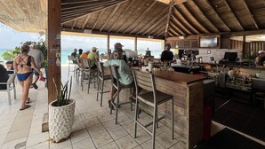 A covered outdoor dining area with a view of the ocean, wooden ceiling, and a bar area with a counter and stools. - Sapphire Beach Retreat - Luxury Oceanfront Gem! (St Thomas)