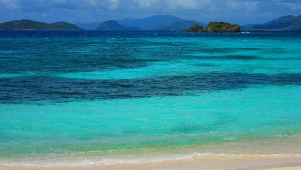 A beach with clear turquoise waters, distant islands, and a cloudy sky. - Sapphire Beach Retreat - Luxury Oceanfront Gem! (St Thomas)