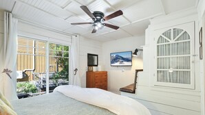 Une chambre à coucher comprenant un lit, un ventilateur de plafond, une commode, un téléviseur et une fenêtre avec des rideaux.