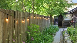 Une clôture en bois décorée de guirlandes lumineuses, un chemin de pierres et de la verdure.