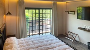 Un dormitorio con una cama grande, una ventana con cortinas, una mesita pequeña y un espejo en la pared.