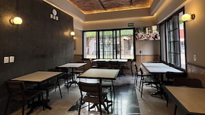 Un comedor moderno con varias mesas y sillas, techo de madera y grandes ventanales que permiten la entrada de luz natural.