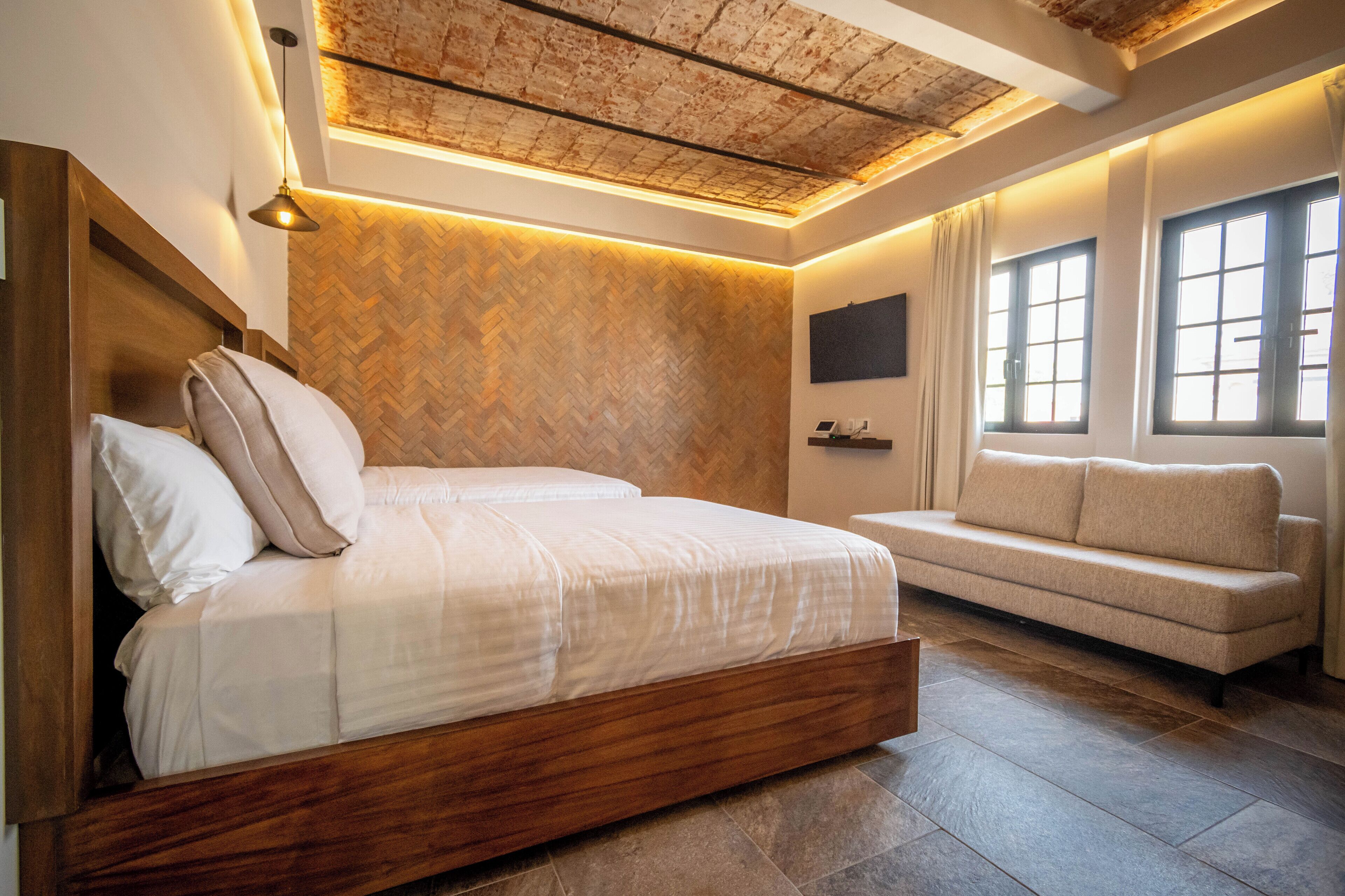 Un dormitorio moderno con una cama de madera, un sofá, un revestimiento de pared con motivo de espiga y un techo con vigas a la vista.