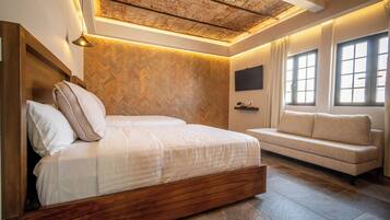 Un dormitorio moderno con una cama de madera, un sofá, un revestimiento de pared con motivo de espiga y un techo con vigas a la vista.