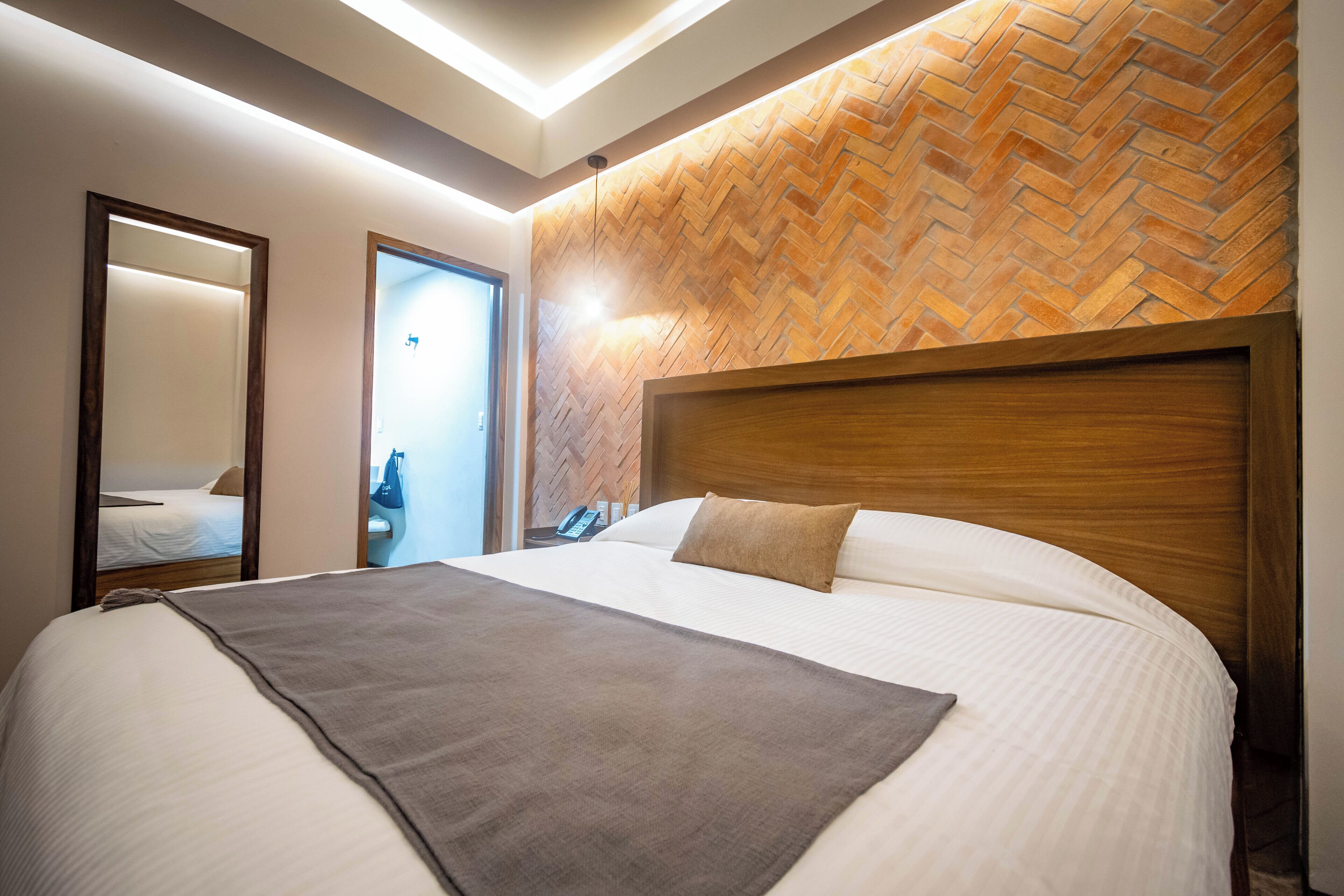 Una habitación de hotel con una cama grande, cabecero de madera y una pared con estampado de espiga.