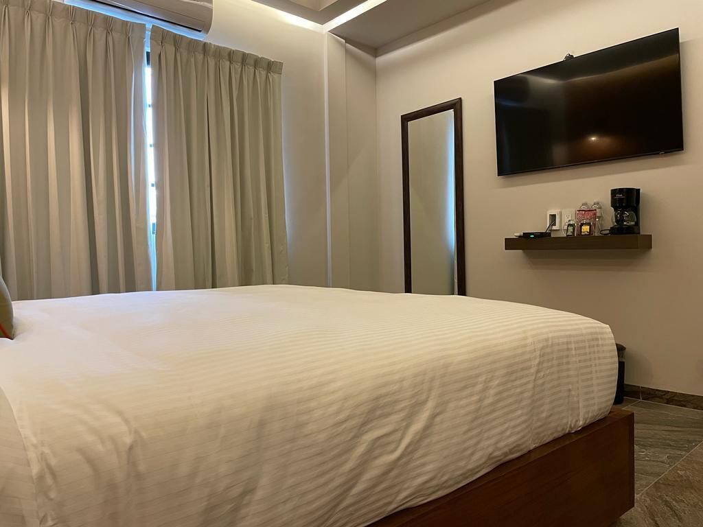 Una habitación de hotel con una cama, un televisor montado en la pared y una cafetera en un estante.