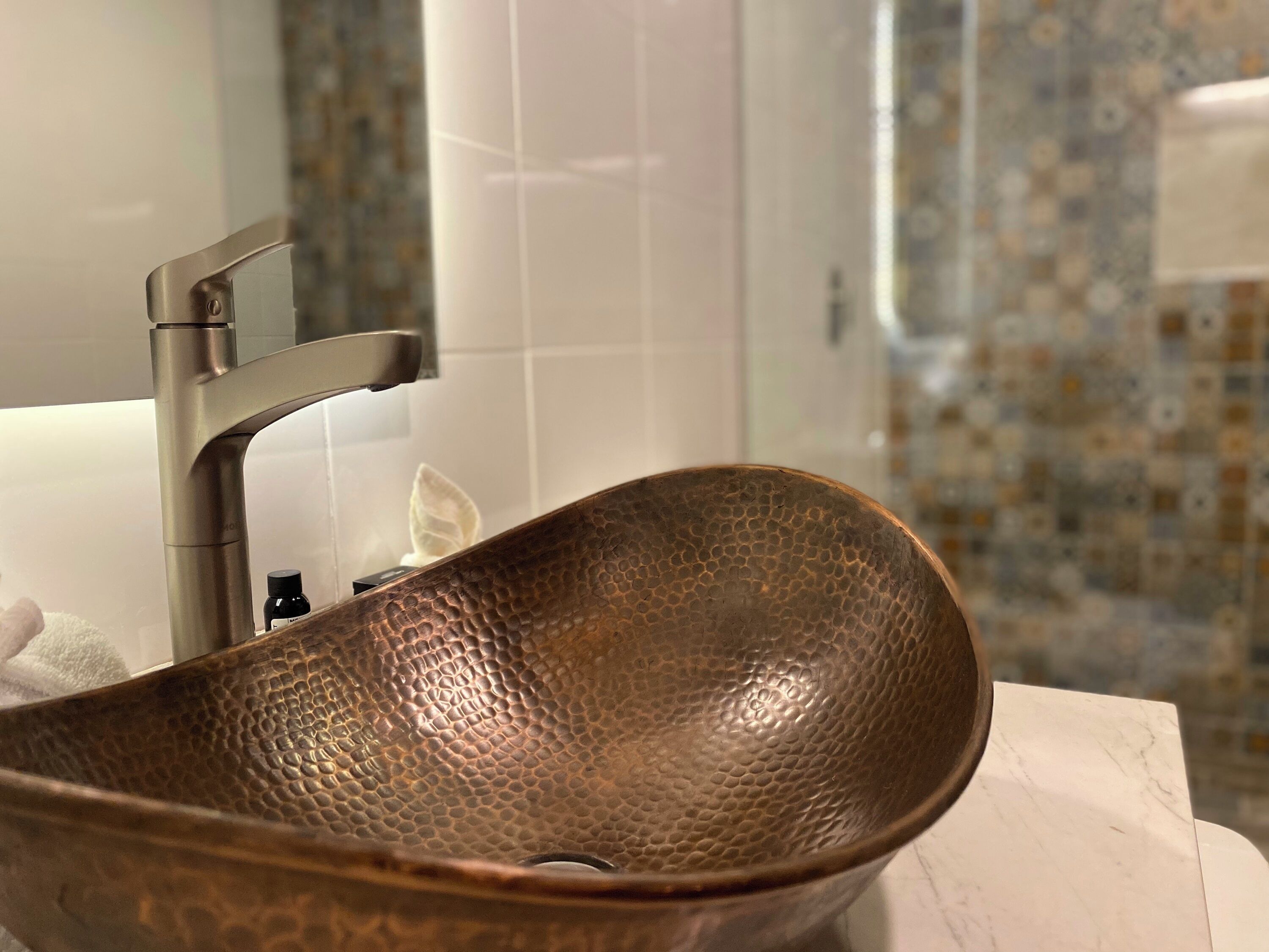 A bathroom with a copper sink, white tiles, and a patterned tile backsplash.