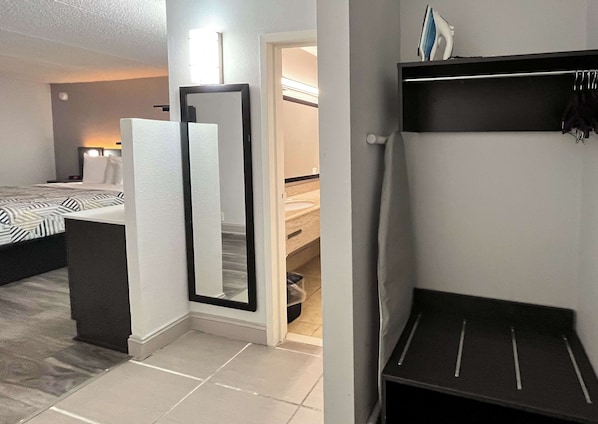 A hotel room with a bed, a mirror, a small table, and a closet with shelves.