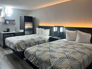 A hotel room with two beds, a kitchenette, and a nightstand with a clock.