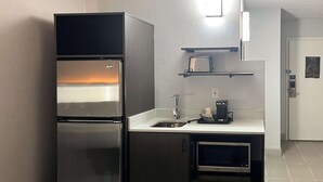 Eine kleine Küche mit einem Edelstahlkühlschrank, einer Kaffeemaschine und einer Mikrowelle.